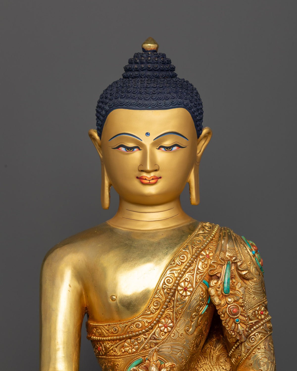 Close-up view of Medicine Buddha statue featuring a serene gold-painted face, semi-precious stones, and detailed monastic robe carvings