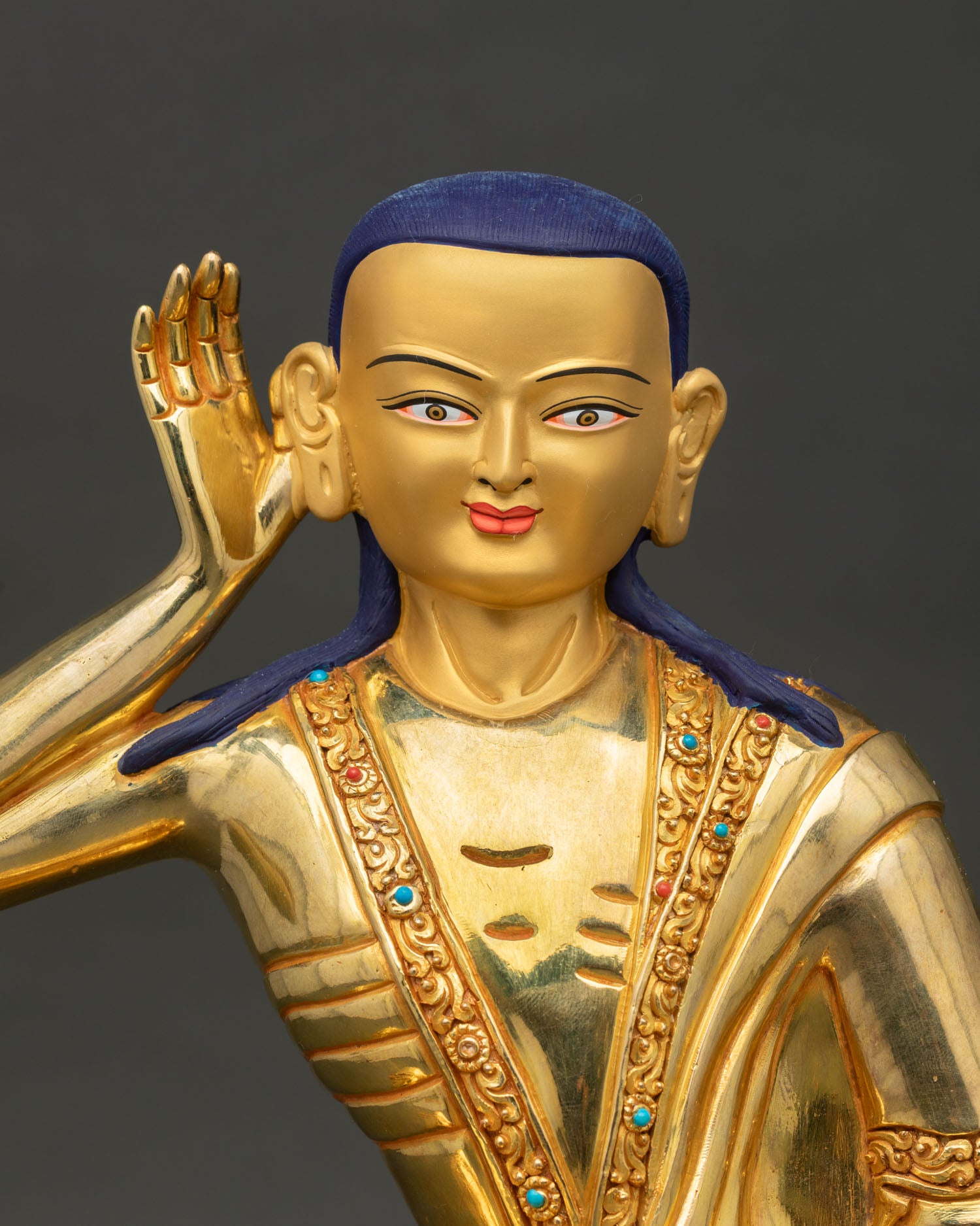 Close up view of Milarepa Buddhist yogi statue, showing gold painted face and intricate robe carvings