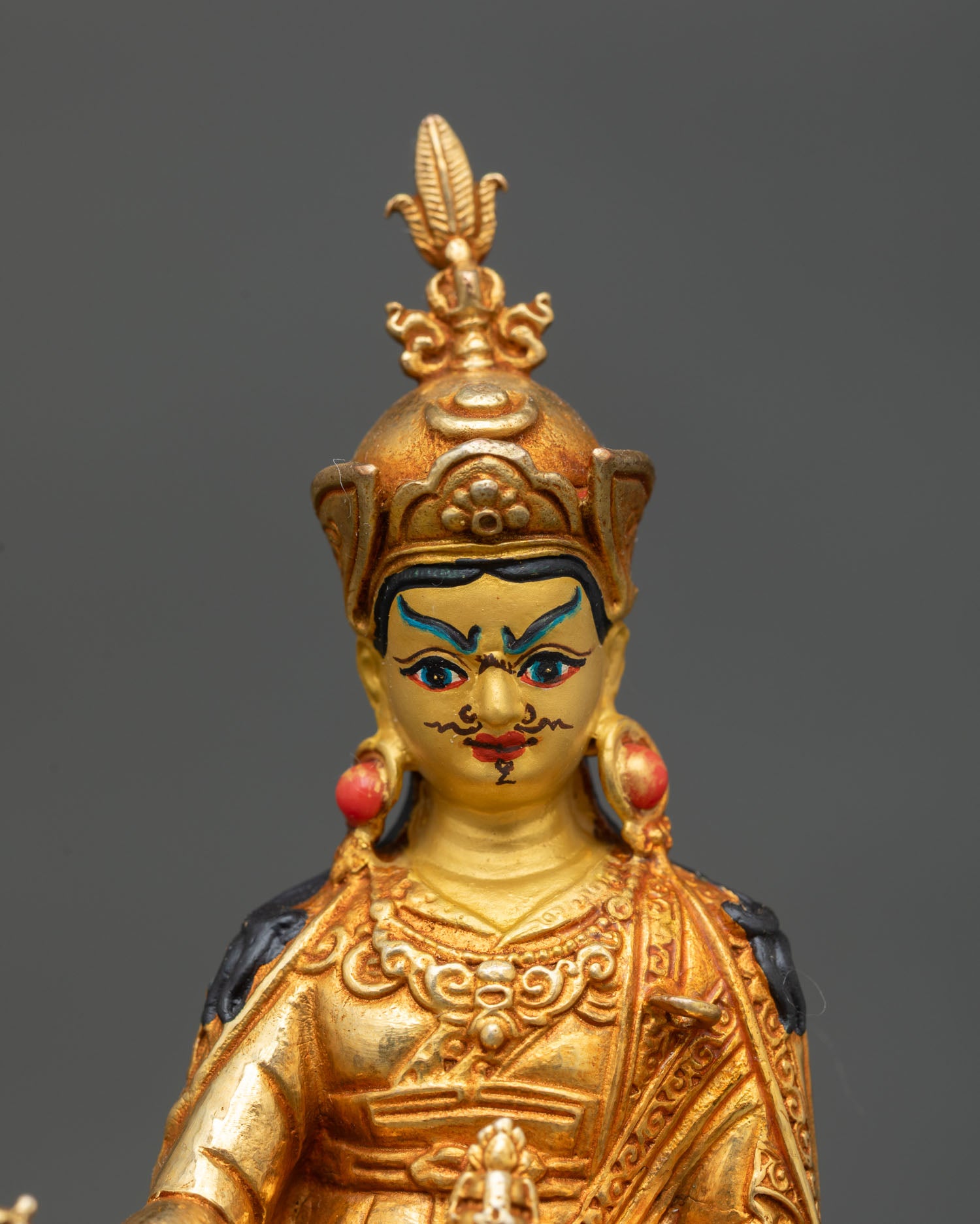 Close-up view of Padmasambhava statue showing expressive facial details, intricate gold craftsmanship on the copper surface
