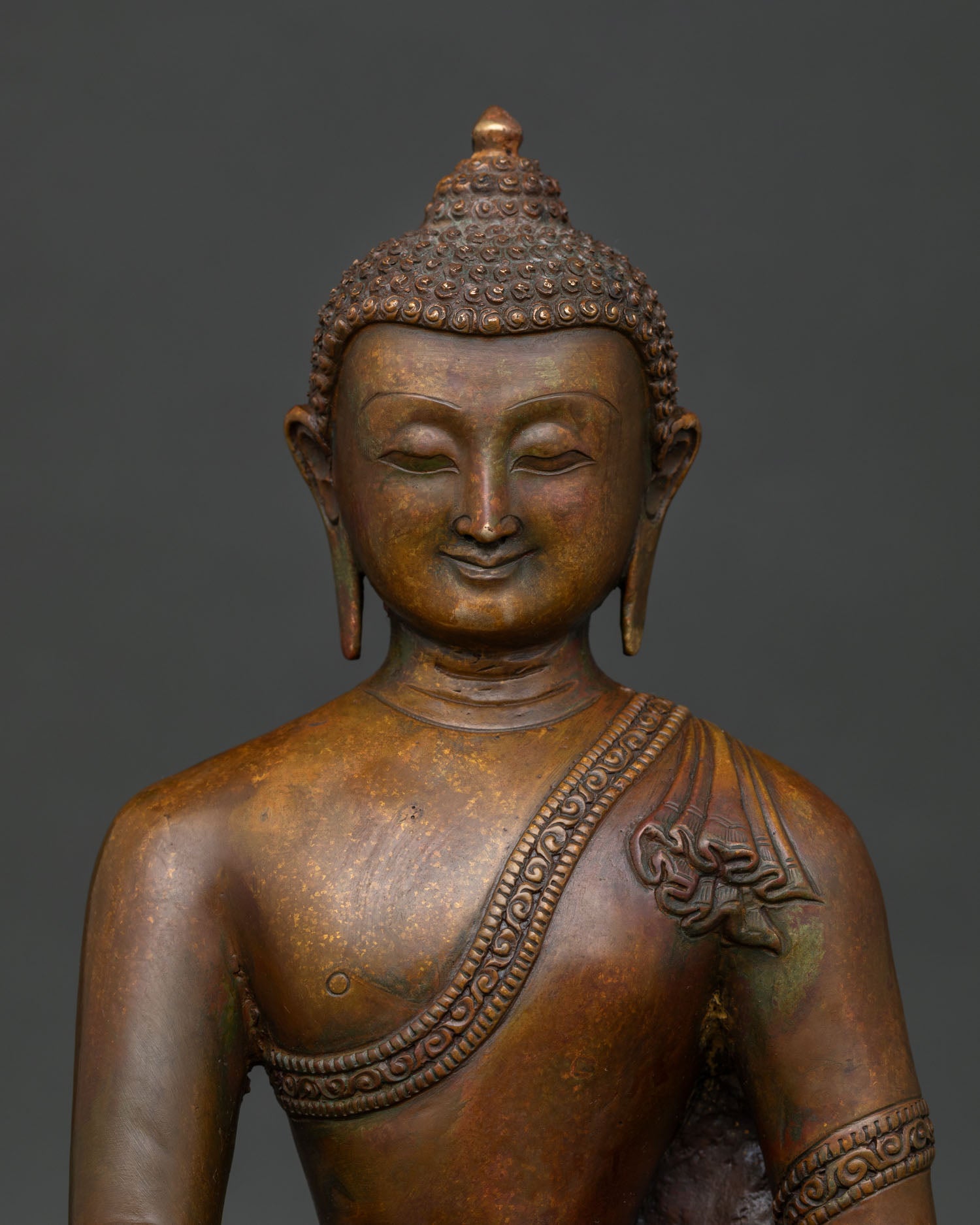 Close up view of Shakyamuni Buddha face with detailed monastic robe carving and antique copper finish.