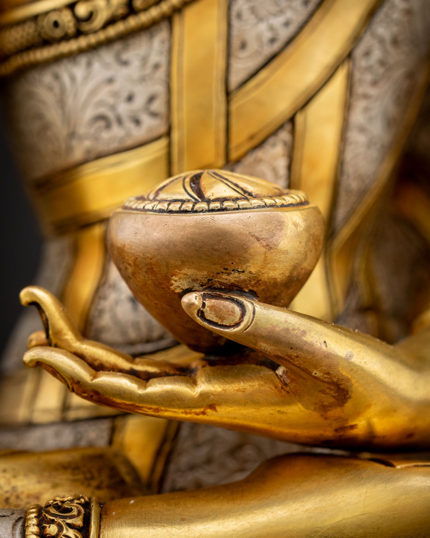 Close-up view of Shakyamuni Buddha left hand holding patra bowl showing detailed copper craftsmanship with gold fire gilded finish and sacred Vajrayana symbolism