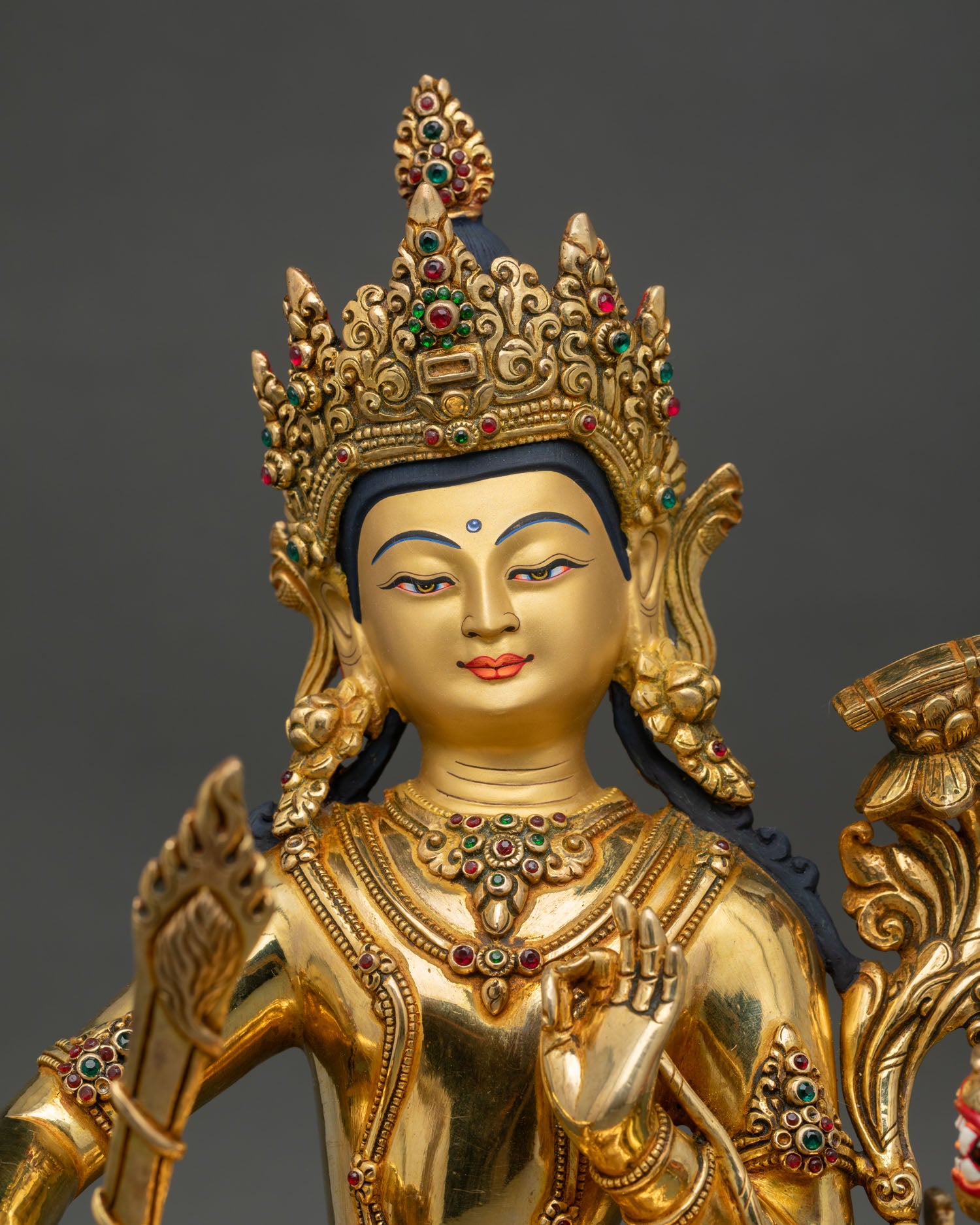 Close up view of Simhanada Manjushree statue, highlighting serene gold gilded face, flaming sword of wisdom and utpala flower with Prajnaparamita Sutra detail.