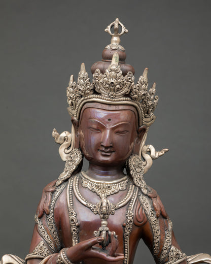 Close up view Vajrasattva face in serene meditation expression holding vajra and bell near heart in silver plated copper Buddhist sculpture
