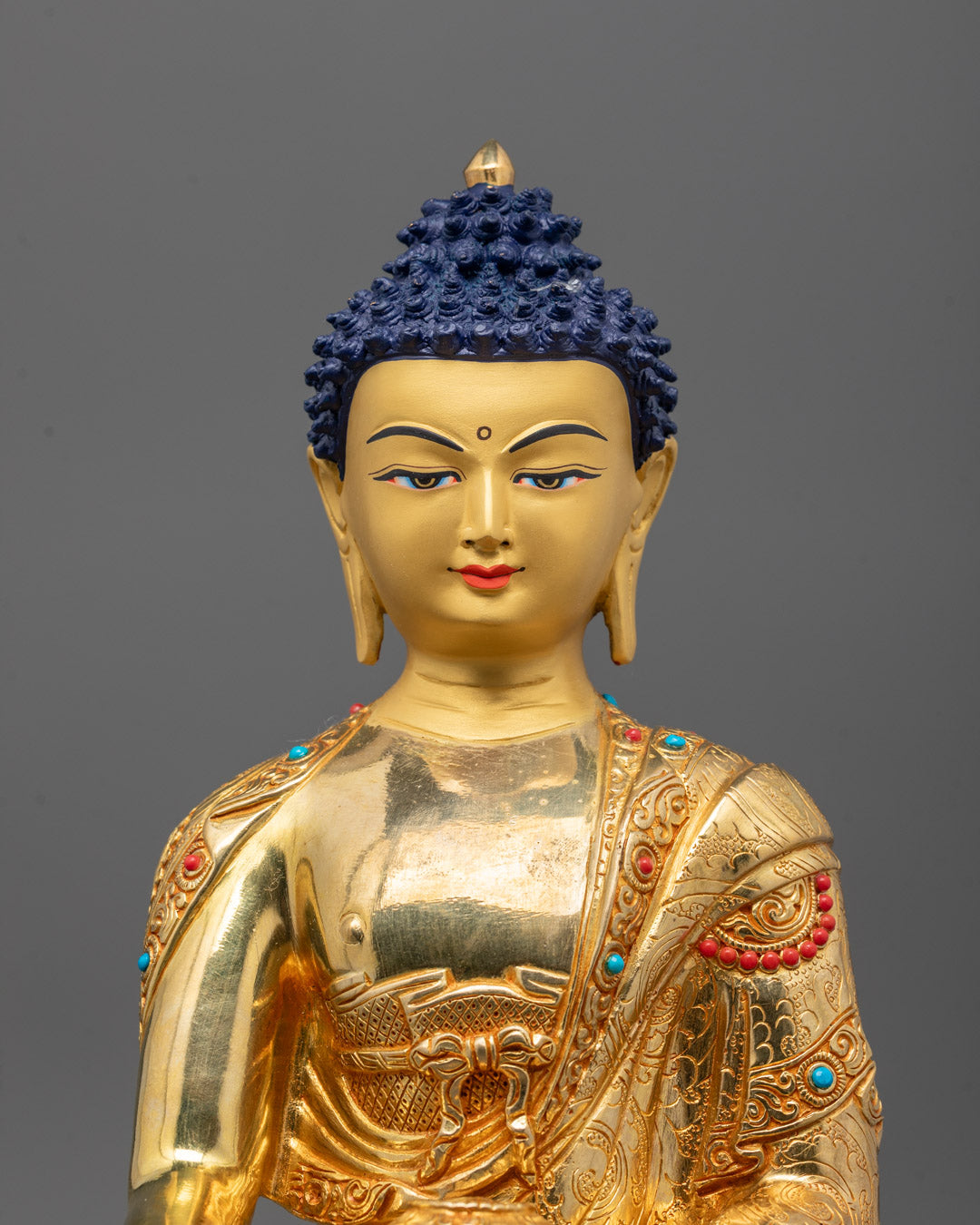 close-up of Shakyamuni Buddha’s gold-gilded face and stone-inlaid robe details from Patan, Nepal
