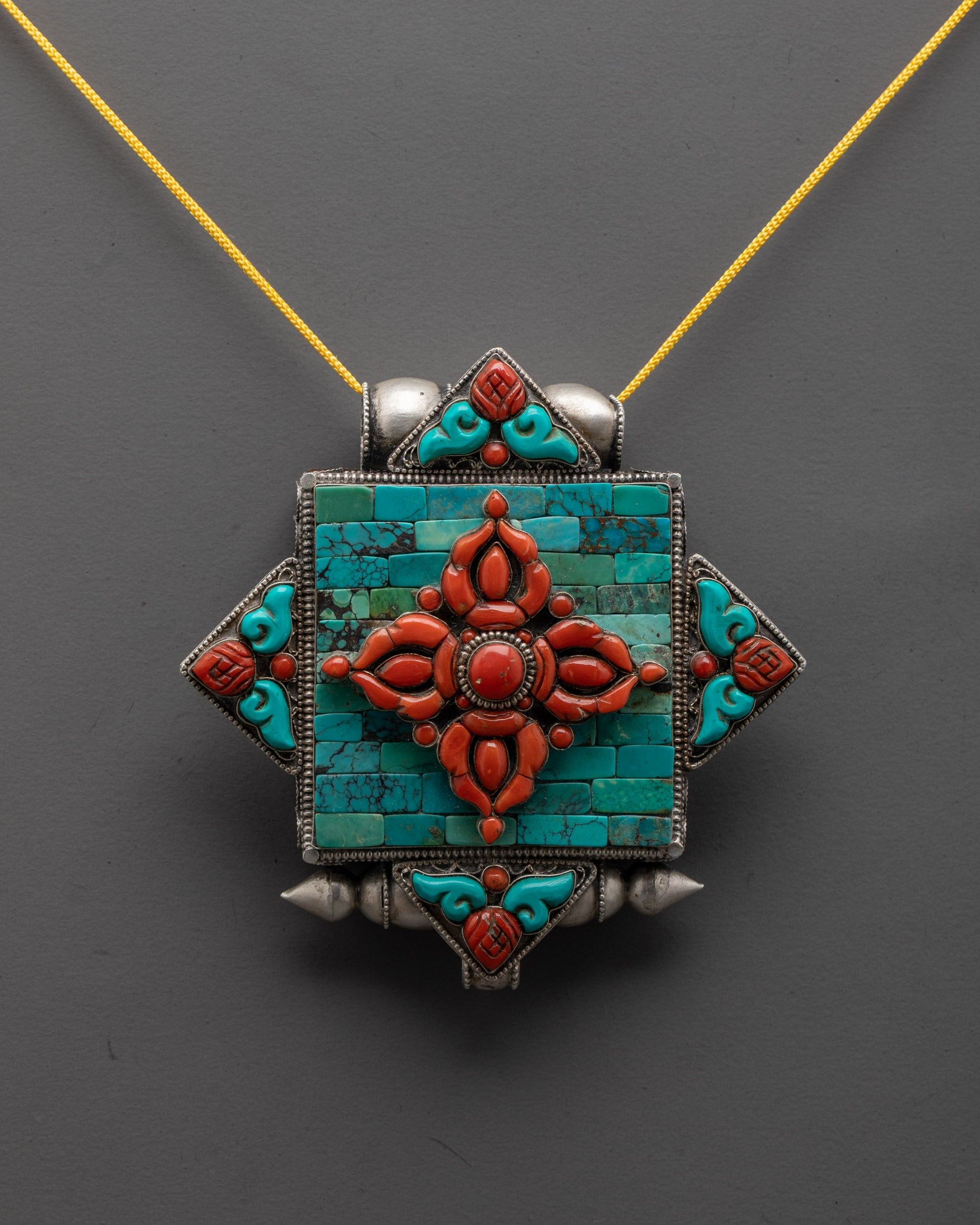 close-up of coral Double Vajra symbol on intricately carved silver locket
