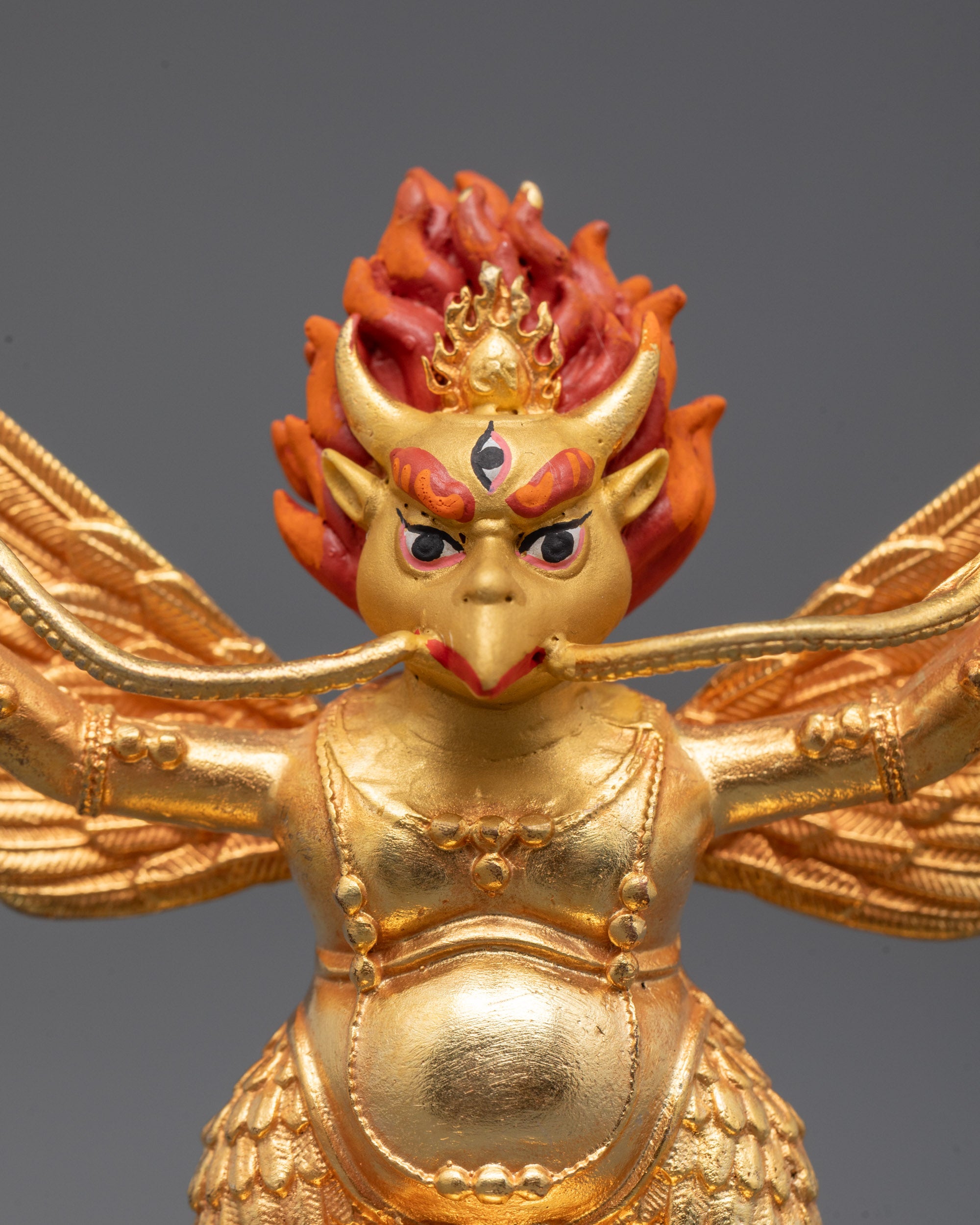 close-up of gold-gilded face and carved jewelry on garuda statue
