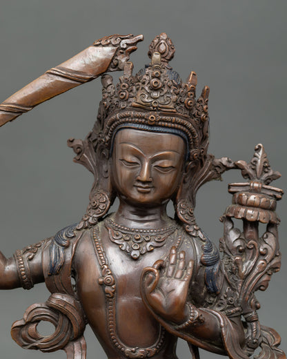 Close view of Manjushri Bodhisattva showing intricate craftsmanship, oxidized copper finish, and serene expression.