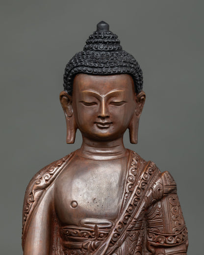 Close view of Shakyamuni Buddha face in oxidized copper showing detailed hand carved robes and fine Himalayan Buddhist artistry.