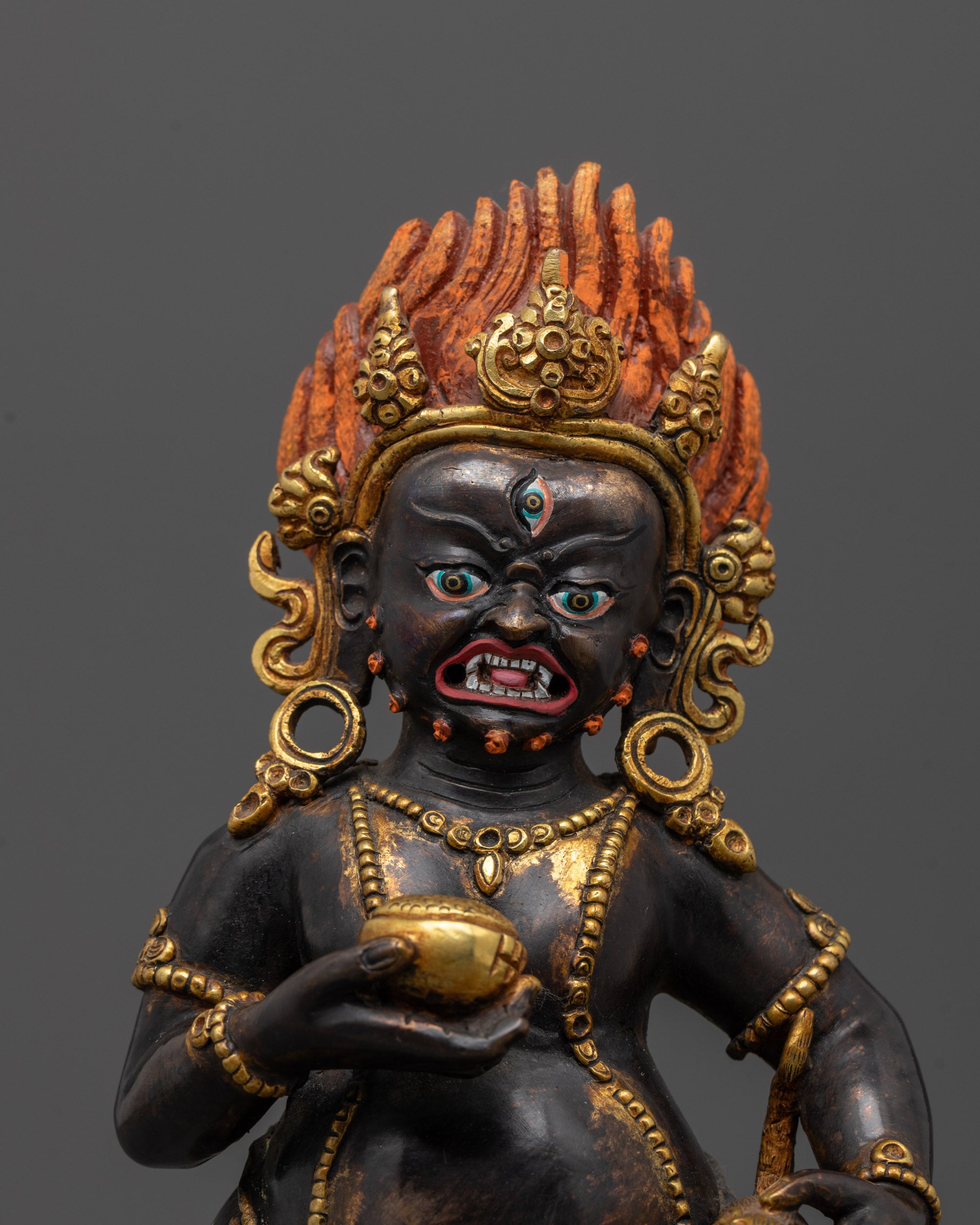 close up of black dzambhala face with third eye and jeweled gold crown