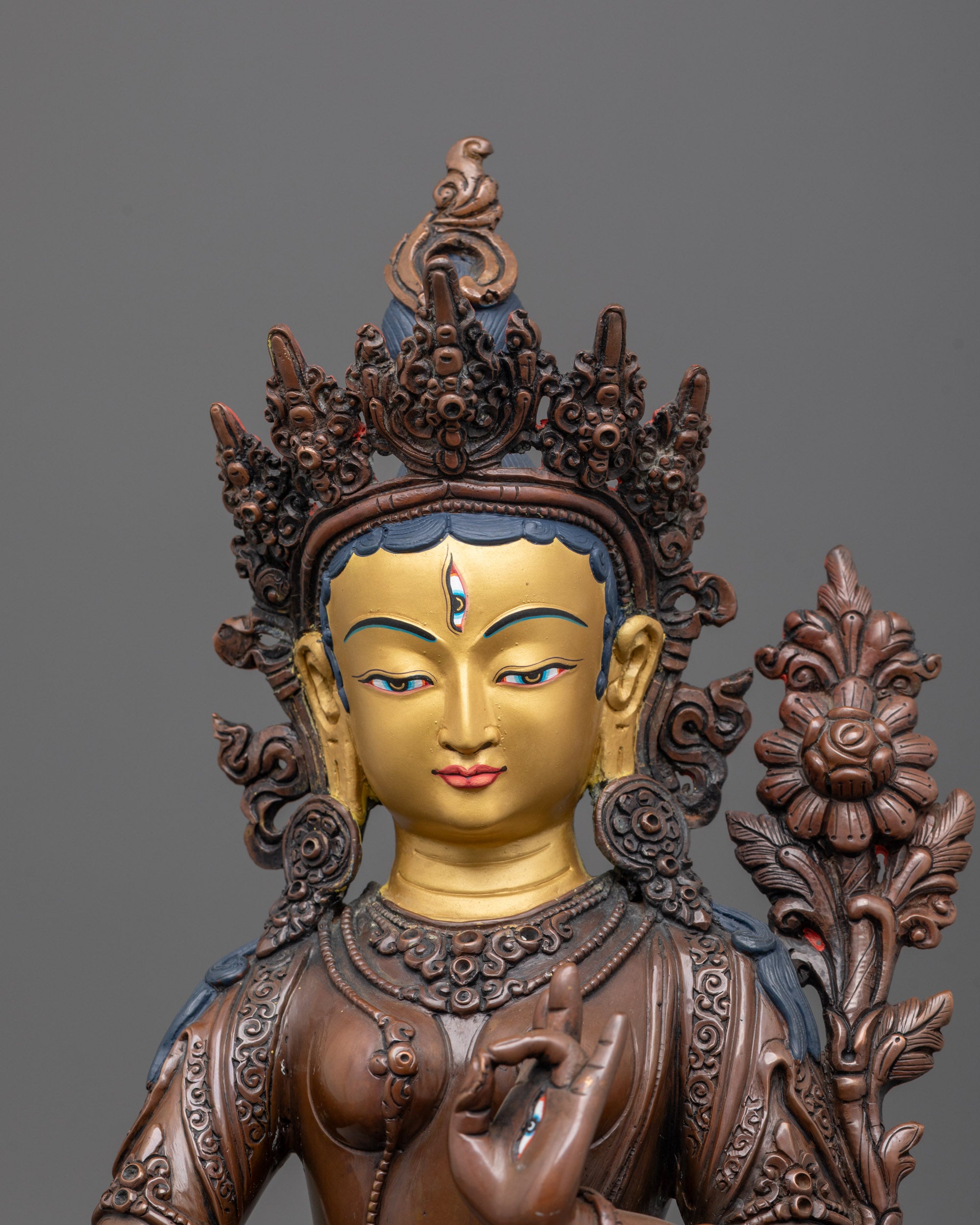close up of gold-gilded face and utpala flower details of white tara oxidized statue