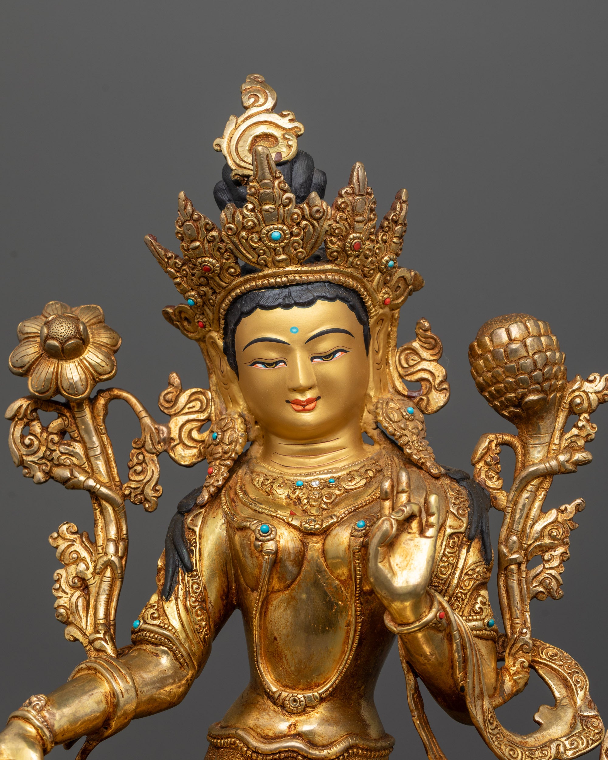 close up of green tara statue showing gold gilded face and intricate crown details
