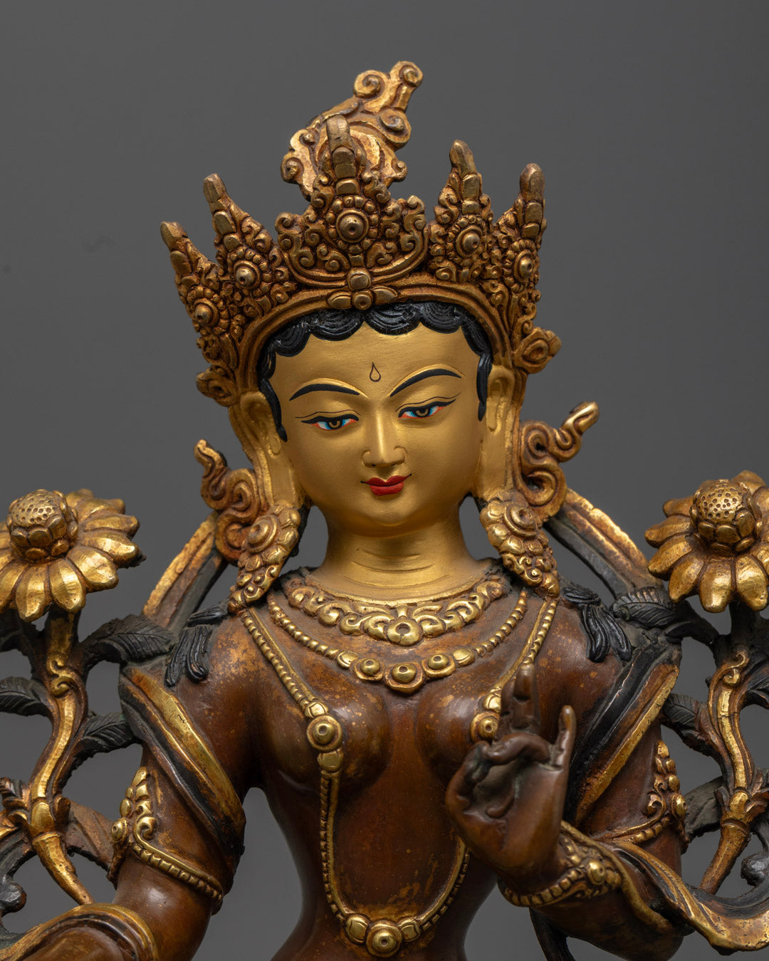 close up of green tara statue with gold-plated robe jeweled crown and serene expression