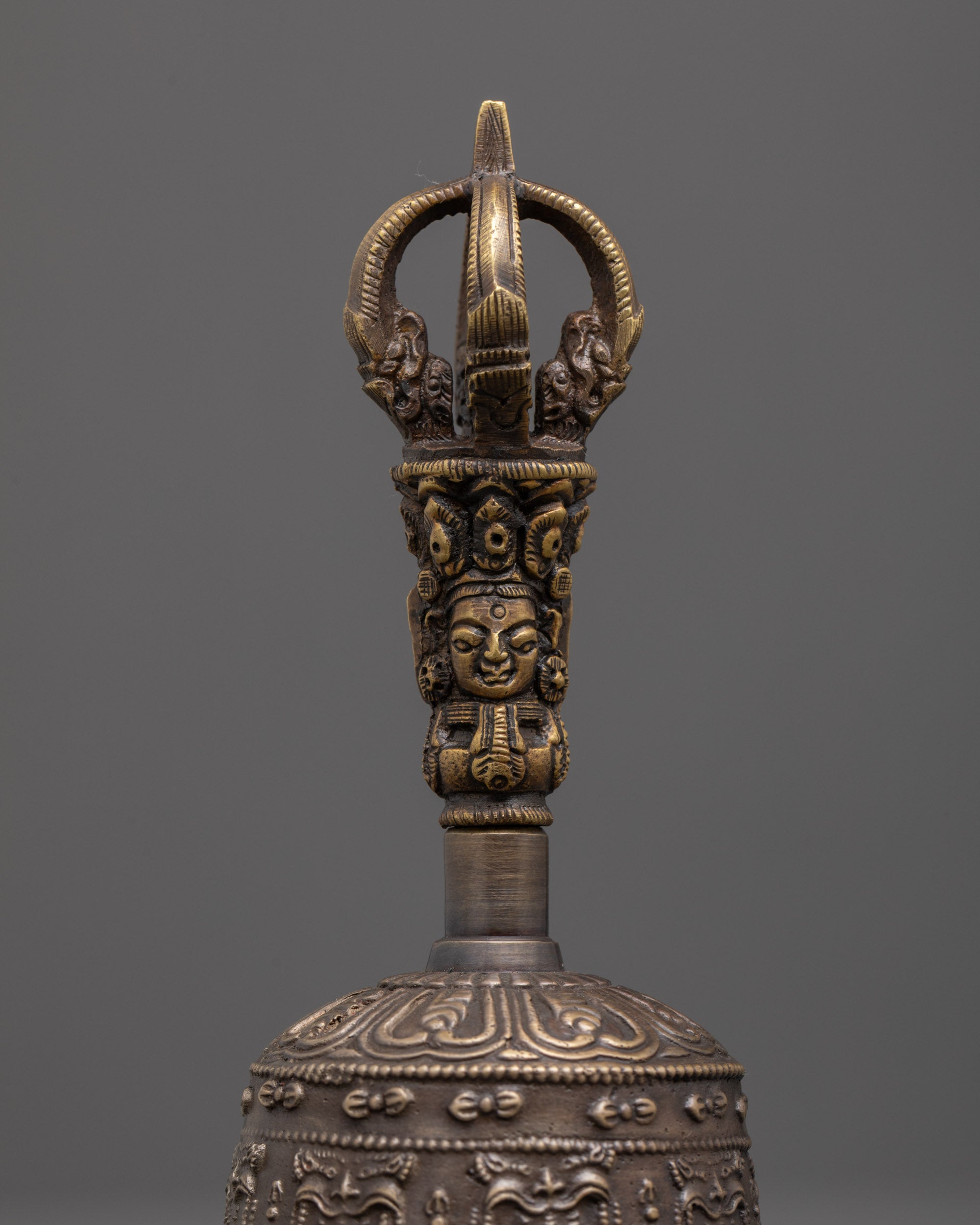 close up of intricate bronze bell carvings with brass handle deity details
