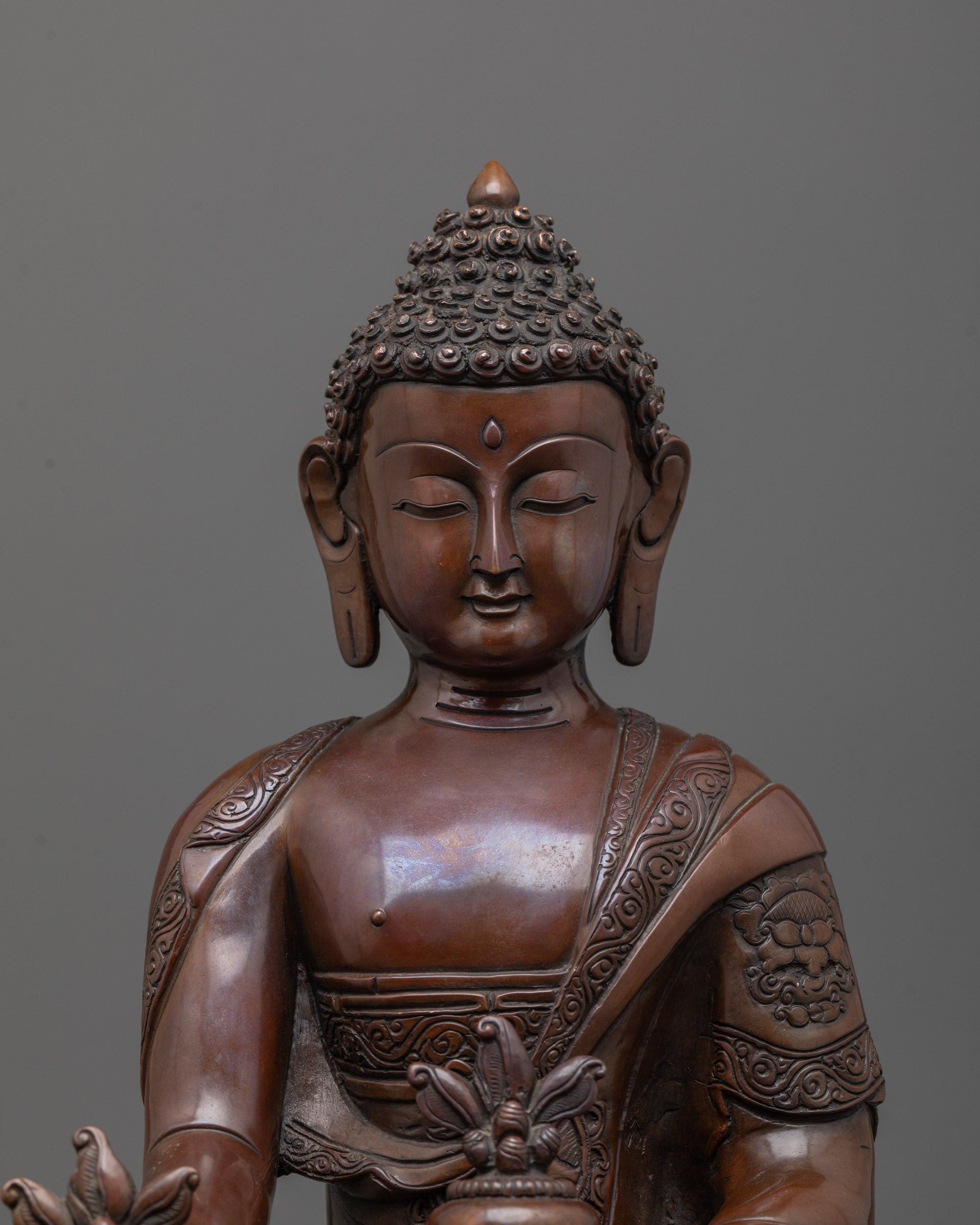 close up of medicine buddha statue holding myrobalan fruit and plant in oxidized copper
