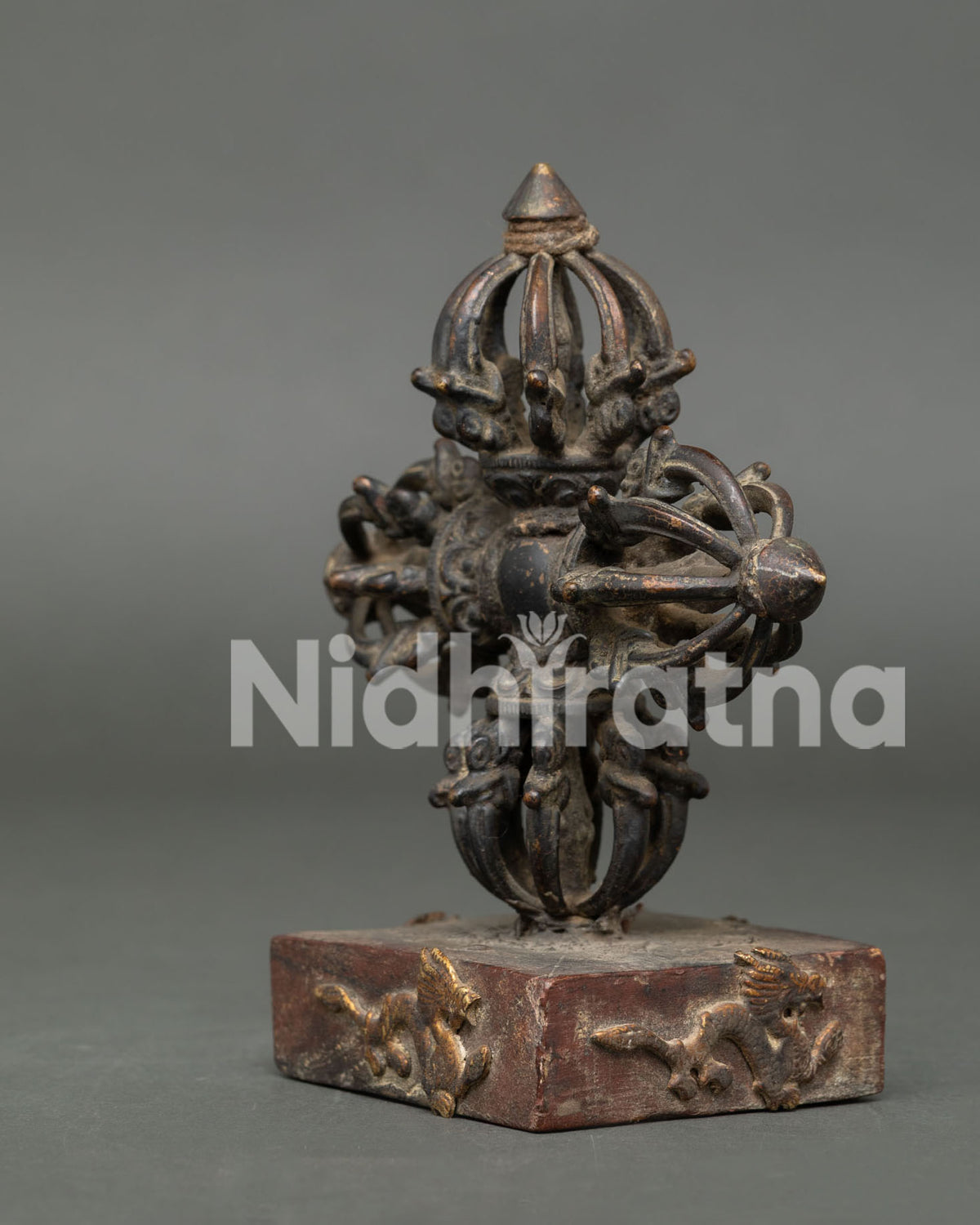 Copper Bishow Vajra with antique finish on rectangular stand with golden dragon motif.