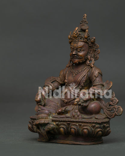 Copper Dzambhala Buddhist wealth deity statue seated on lotus pedestal holding mongoose and citron fruit.