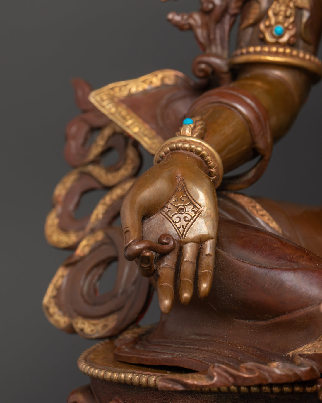 the hand of green tara statue made from copper adorned with turquoise gemstones