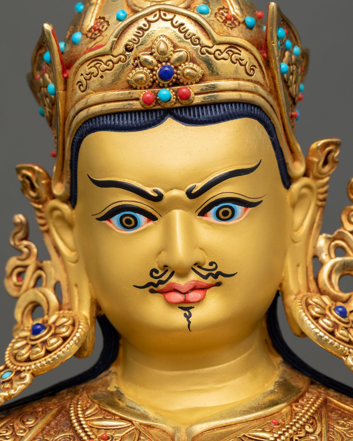 Detailed close-up of Guru Rinpoche face with gold-painted features and delicate carving