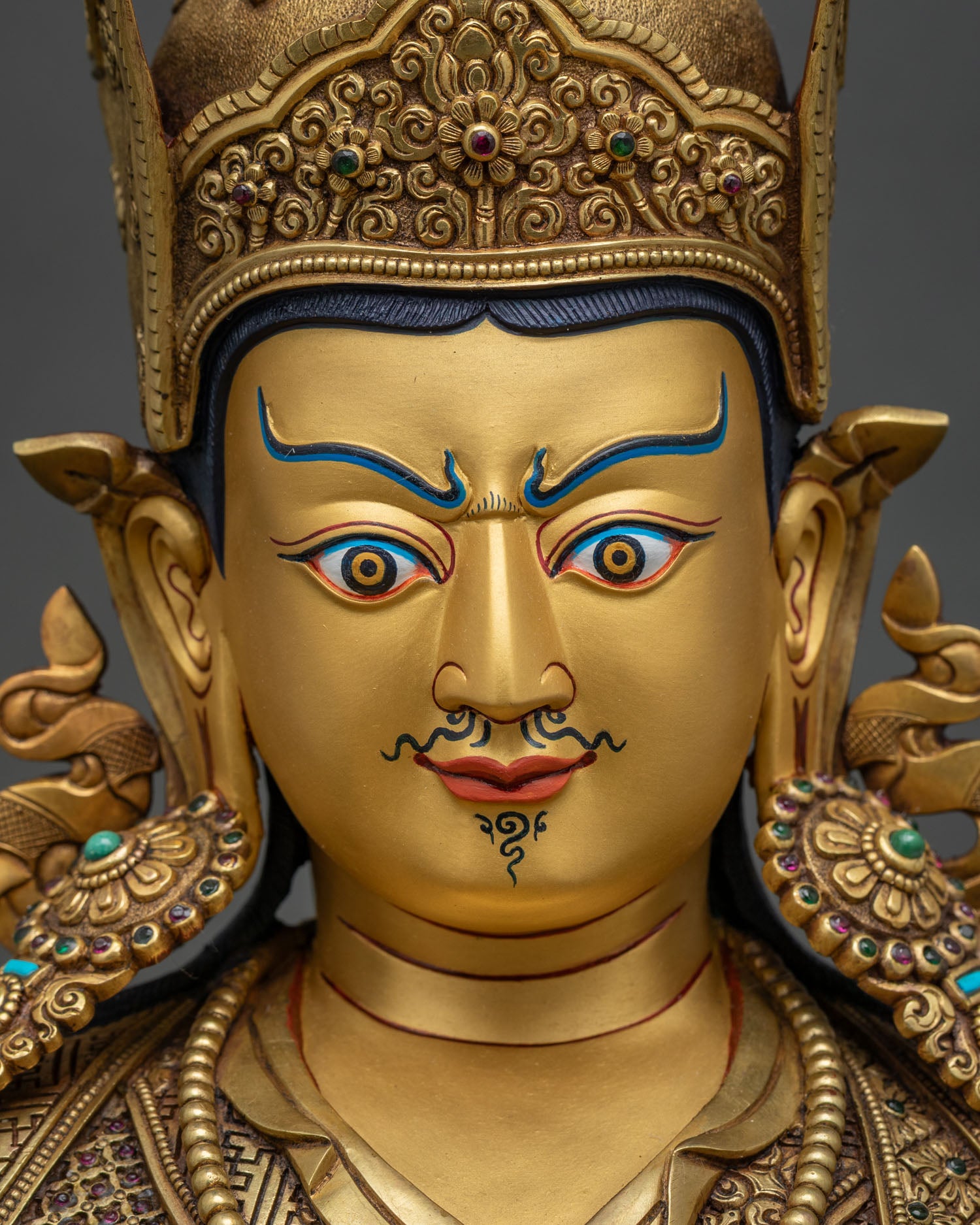 Detailed close-up of 24K gold-painted face on Guru Rinpoche statue