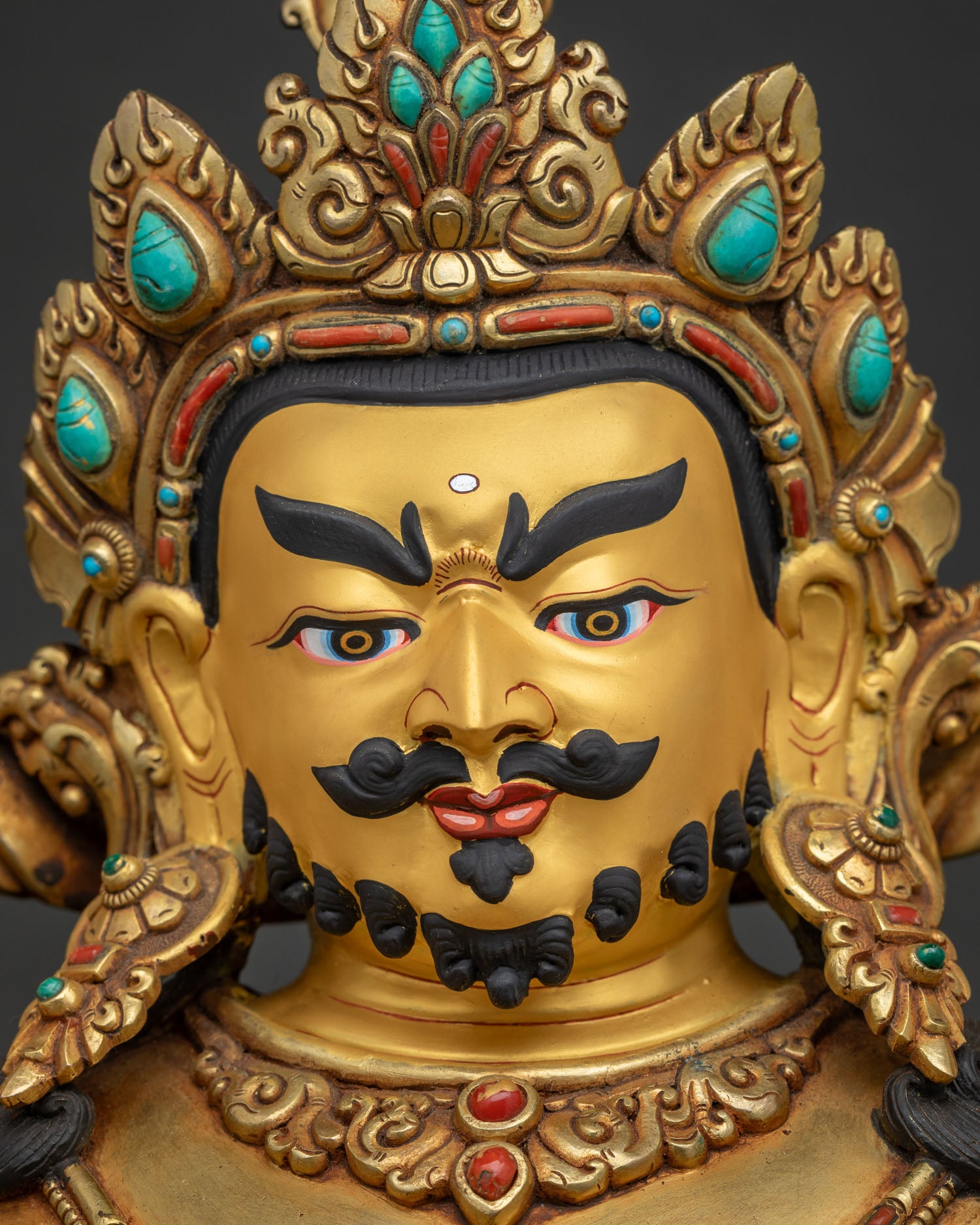 detailed close up of dzambhala face with gold-painted features and ornate crown