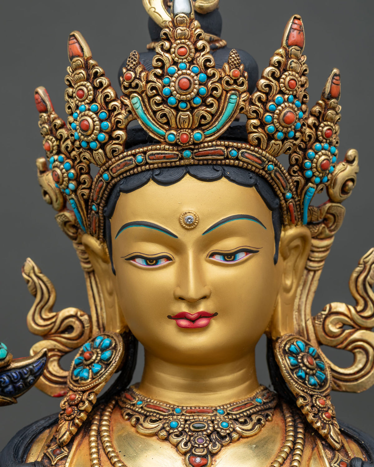 Detailed close up of Green Tara statue face with serene gold-painted expression and jeweled crown