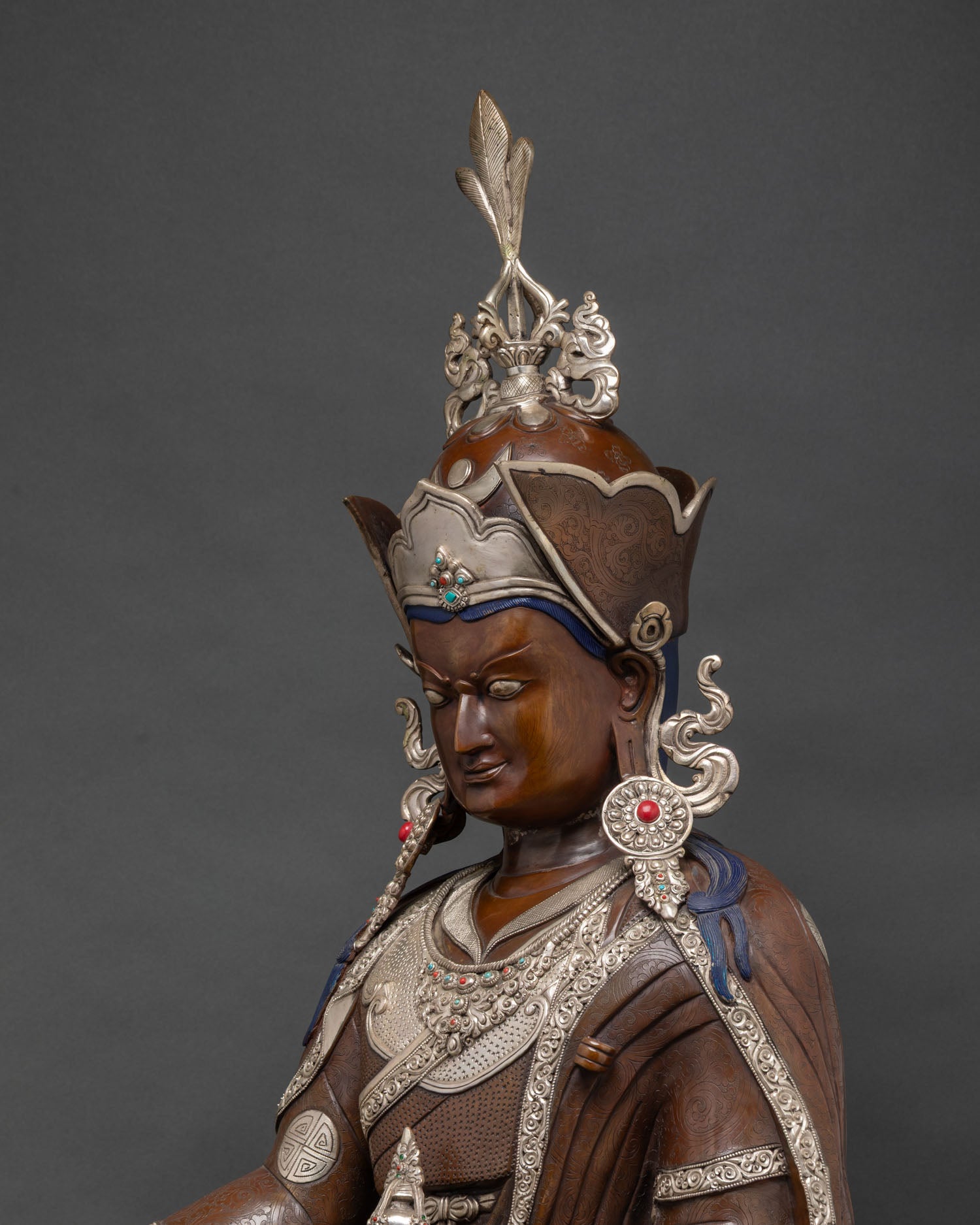 Detailed close-up of Guru Rinpoche face wearing silver-plated lotus hat with gemstones.