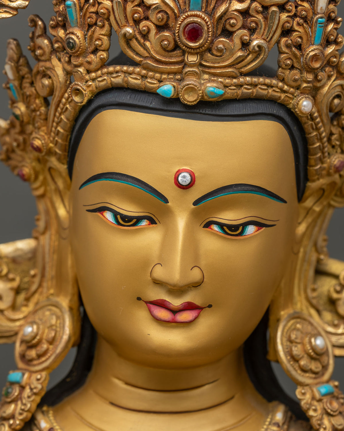 Detailed close up of Manjushri statue face with five-jeweled crown and serene gold-painted features