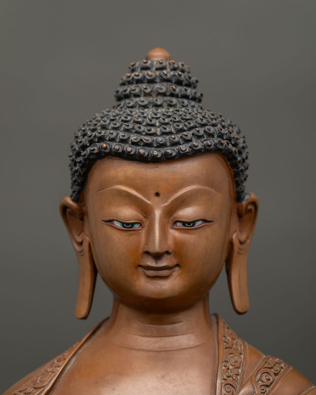 Detailed close up of the face of a Shakyamuni Buddha statue in oxidized copper with brown patina