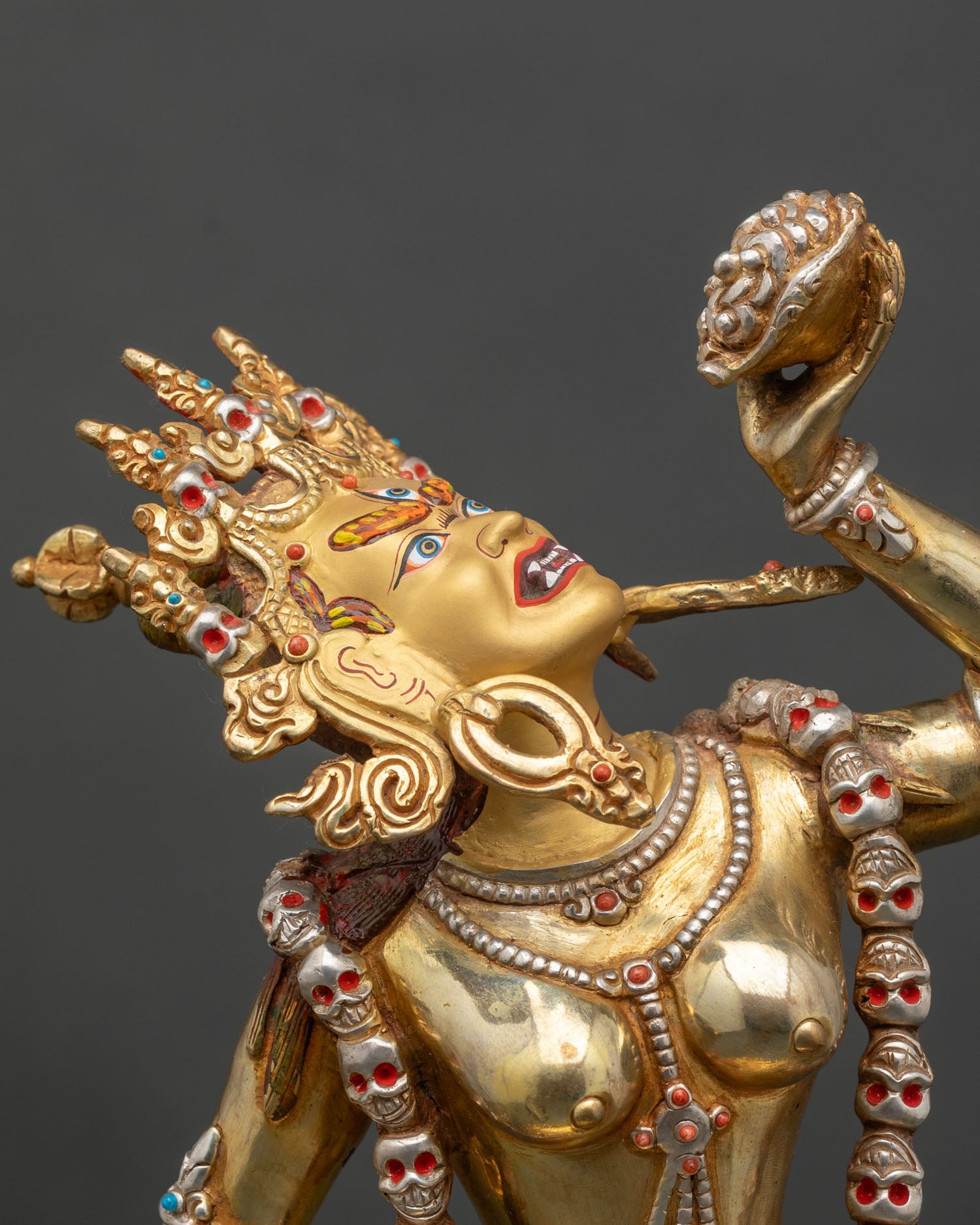 Detailed close-up of Vajrayogini statue face, semi-wrathful expression, gold and gems