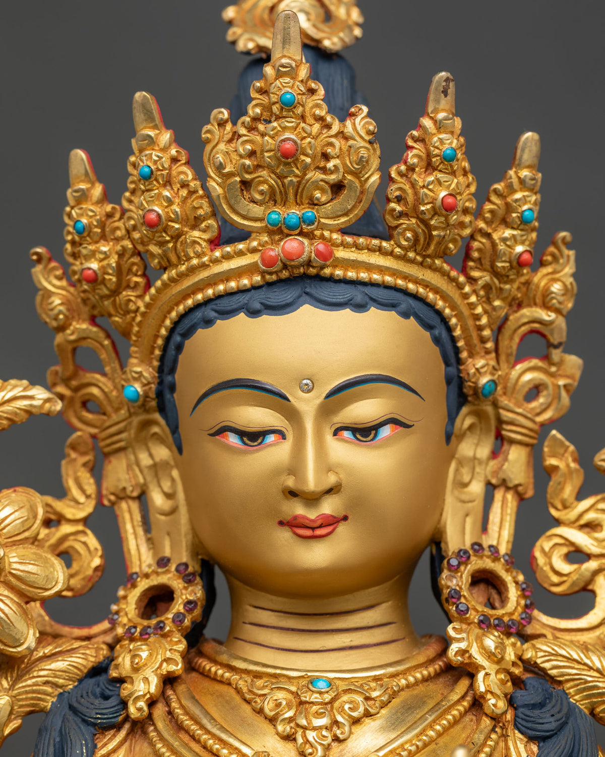 Detailed face of Green Tara statue with serene gold-painted expression and jeweled crown