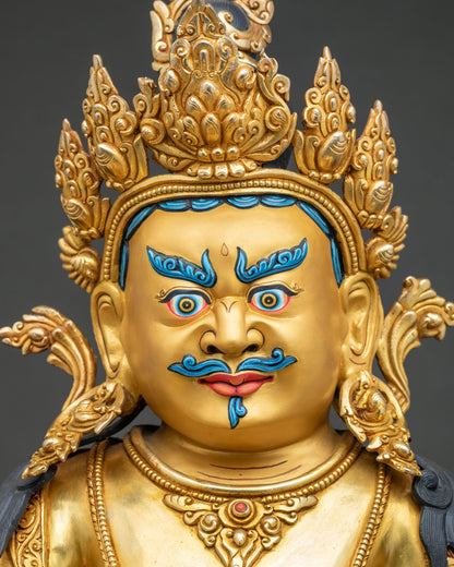 Detailed facial close up of gold gilded Dzambhala statue showing slightly wrathful expression.