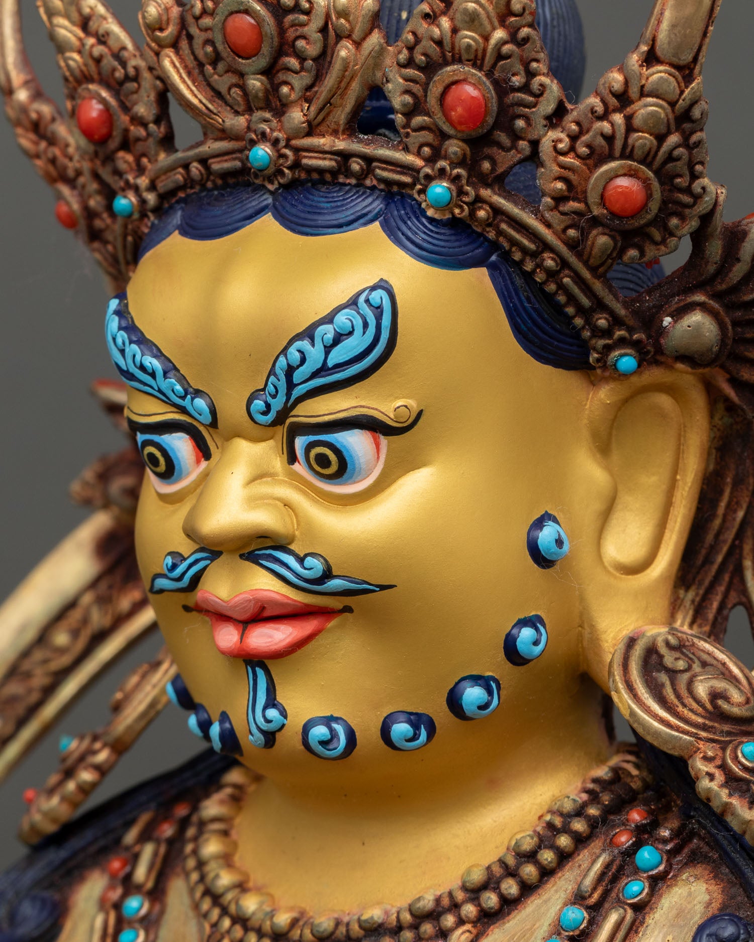 detailed side close up face dzambhala statue showing gold-painted facial features
