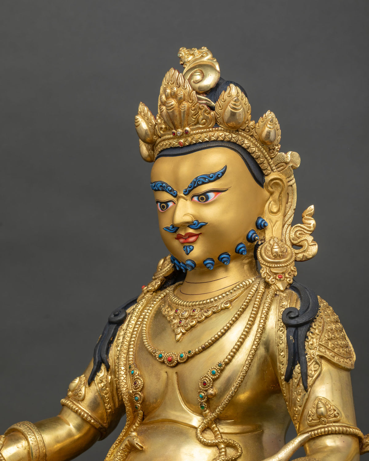 Detailed side close up of gold fire-gilded Dzambhala statue with engraved robes and jewels