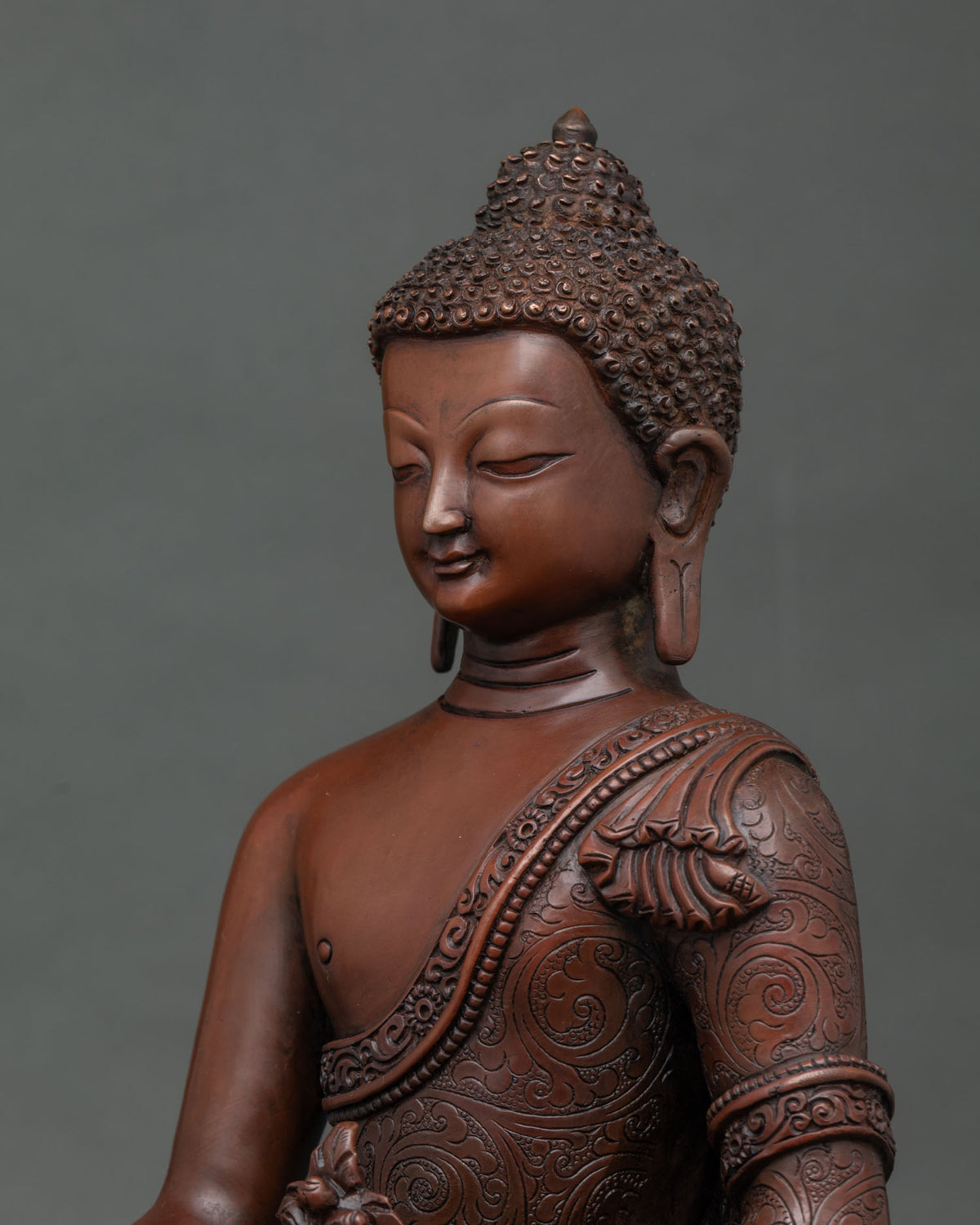 Detailed side close up of swirling floral motifs on robe of copper Medicine Buddha statue