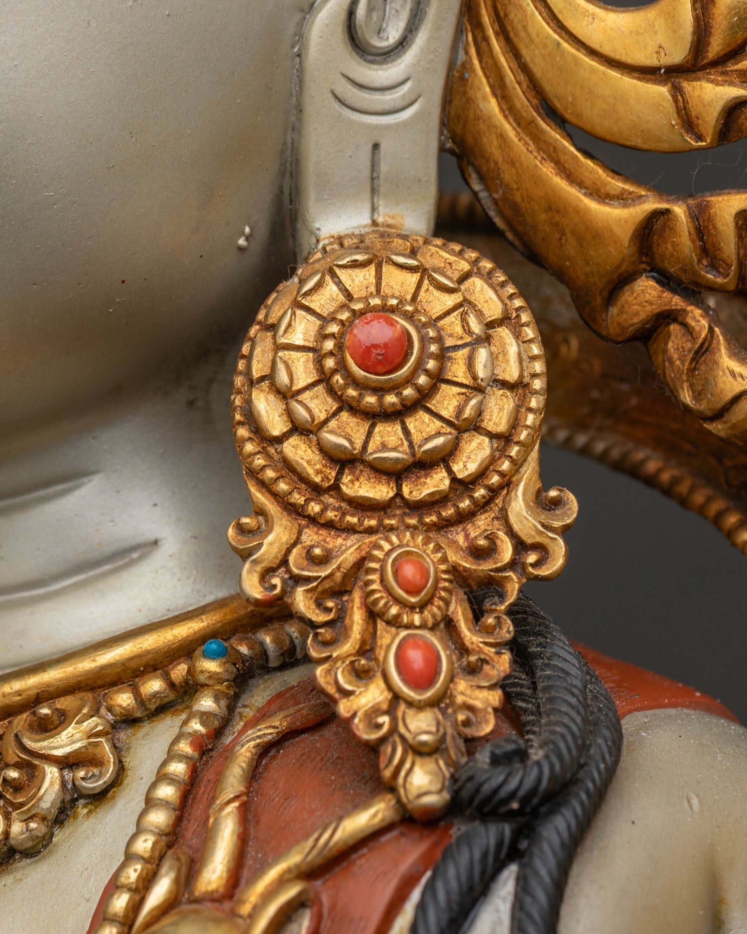 Detailed view of Chenrezig statue's gold earring with coral gemstone inlay