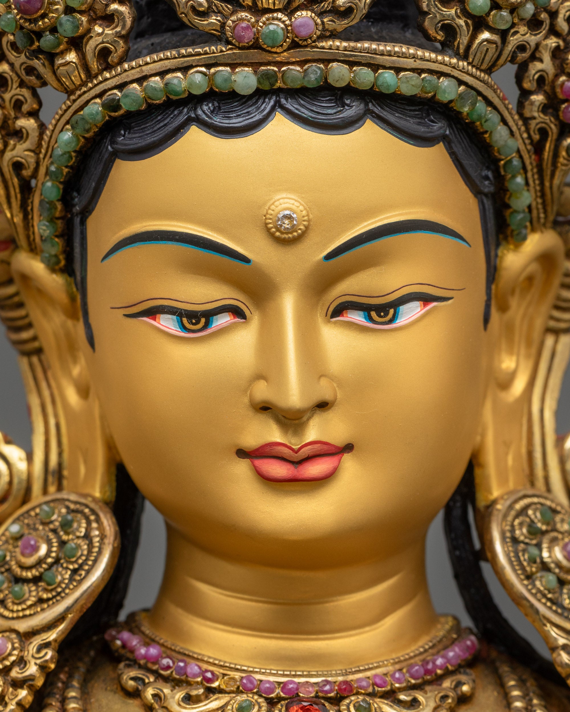 detailed close up face of Green Tara statue with gold-gilded crown and serene expression