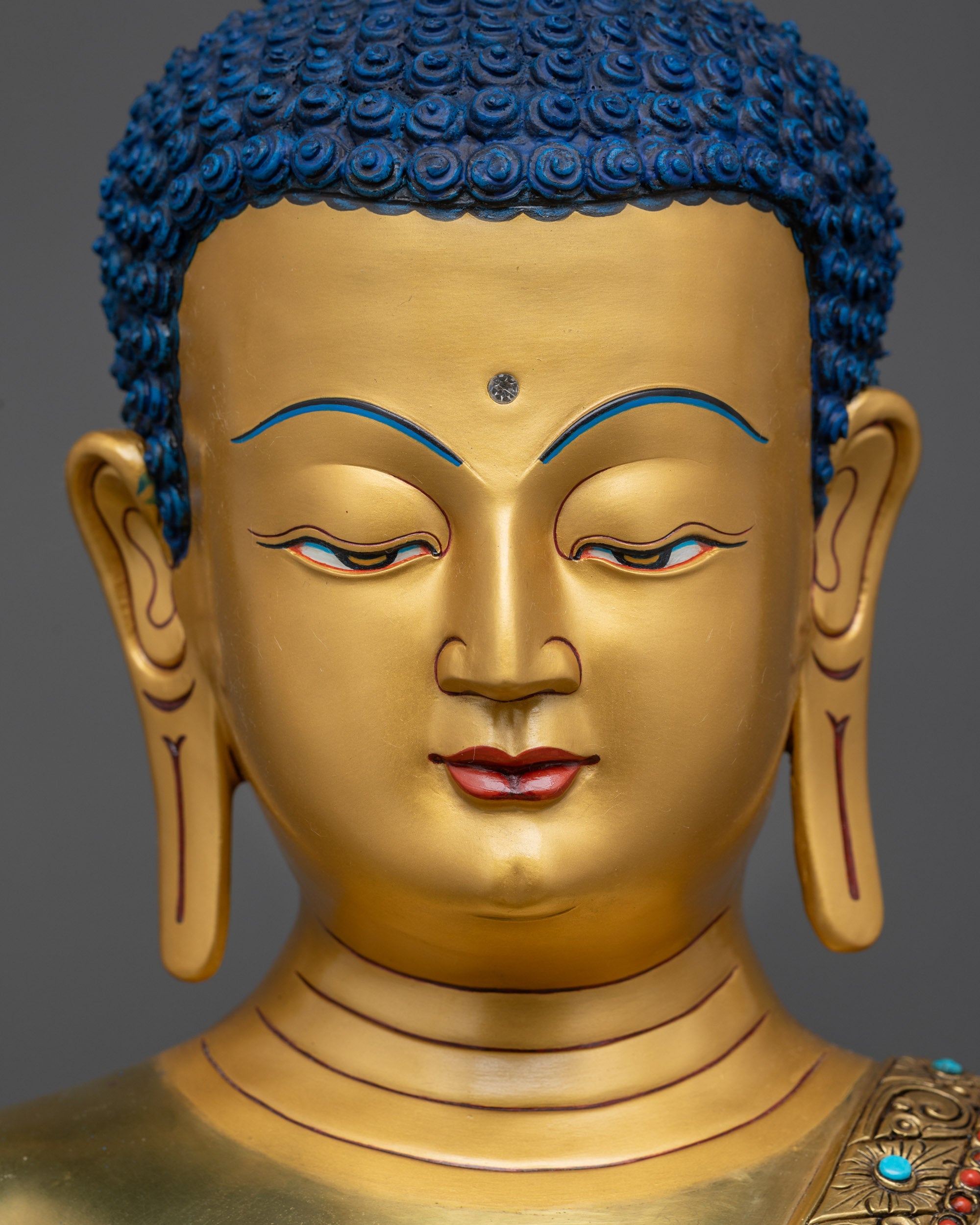 detailed close up face of Medicine Buddha Statue showing serene gold-gilded expression