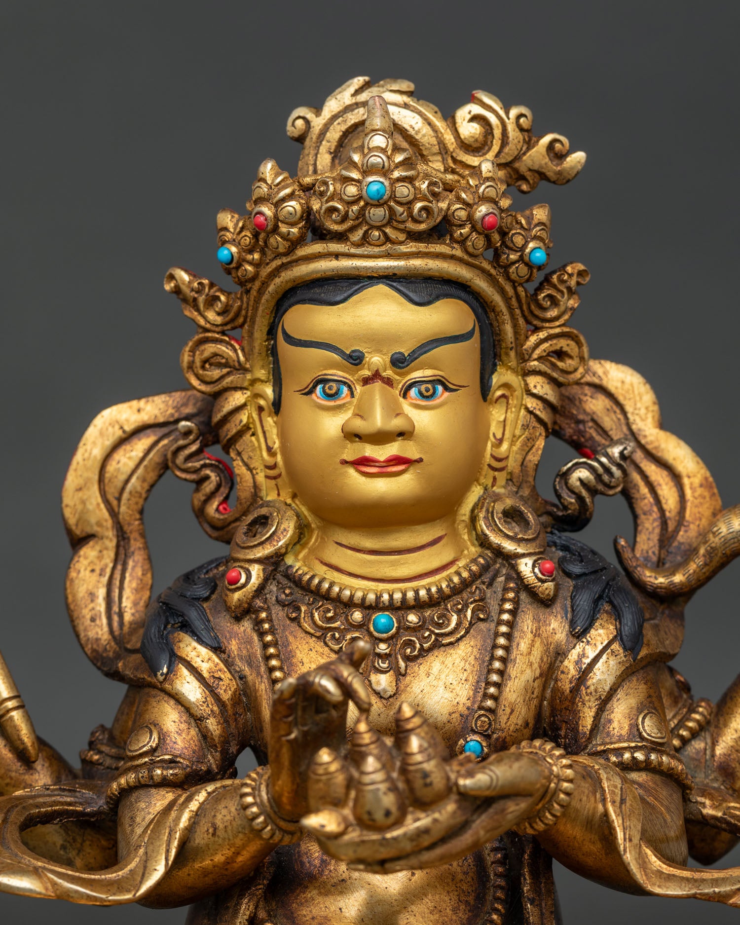 Dzambhala statue close up gold painted face semi precious stone details.