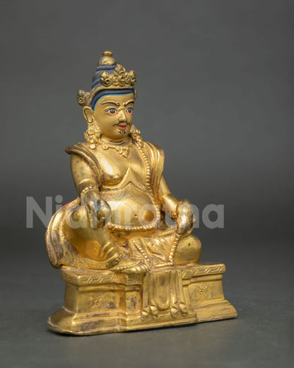 Dzambhala statue holding citron fruit and jewel spitting mongoose side view.