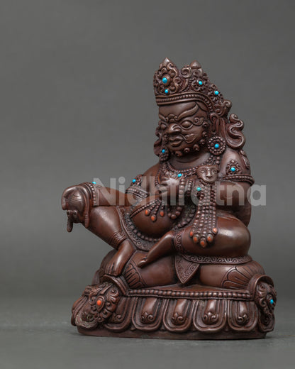 Dzambhala wealth deity statue holding jewel spitting mongoose on carved lotus pedestal.