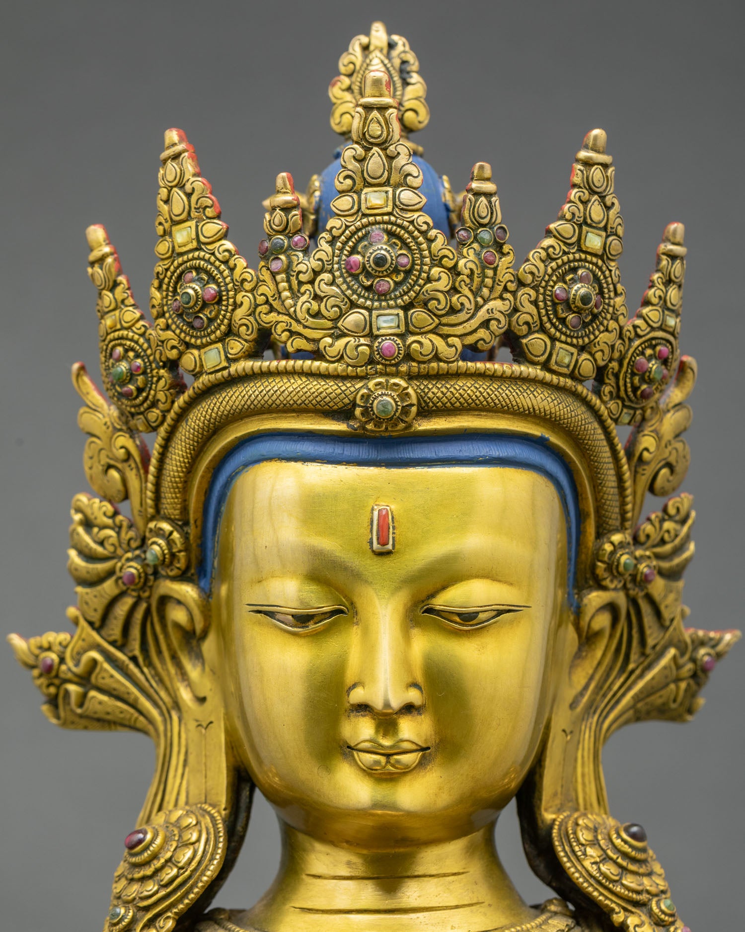 Face close up of Amitayus Buddha statue with serene expression, gold gilding and jeweled crown