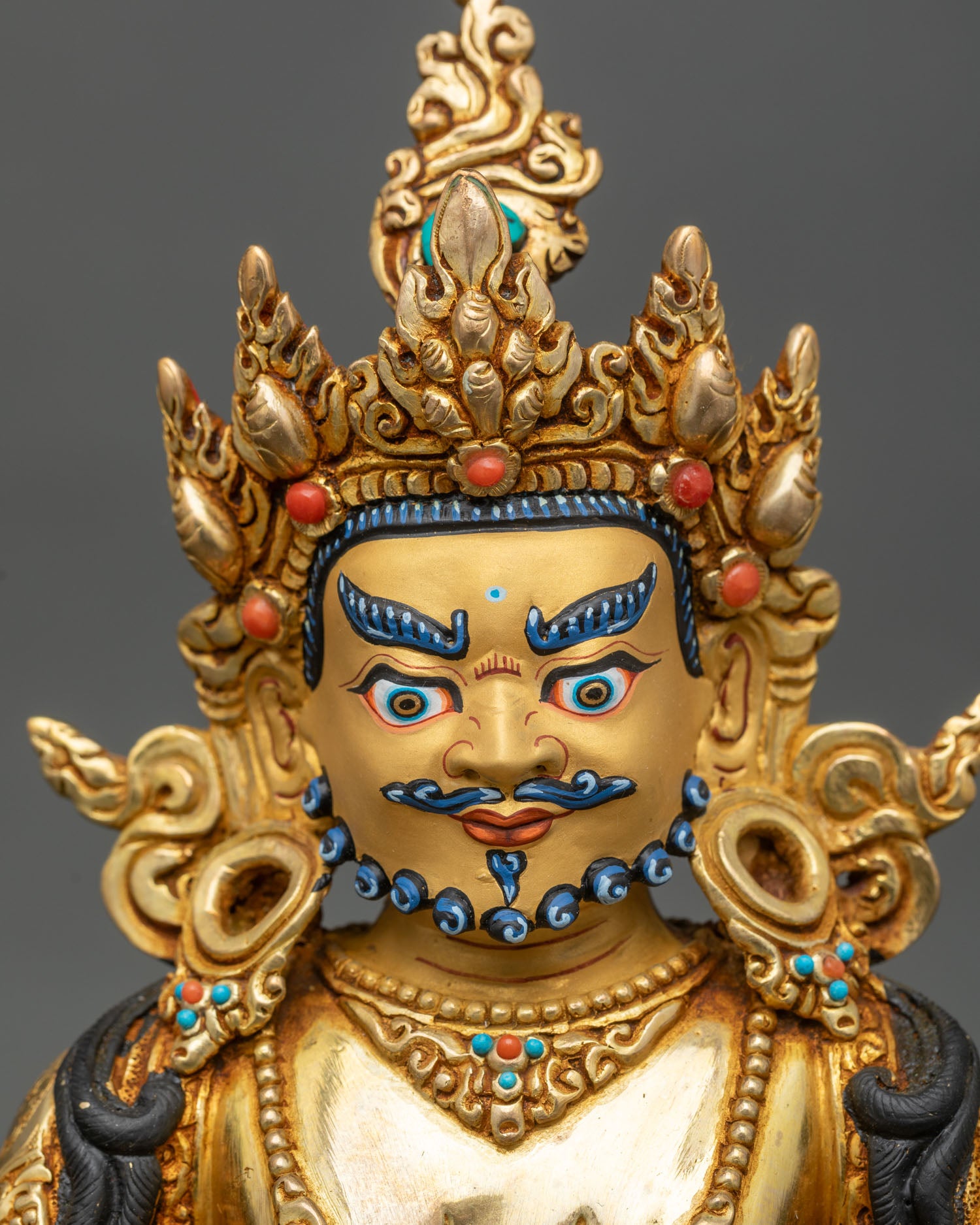 Face close-up of Dzambhala wealth god statue with serene expression and crown details