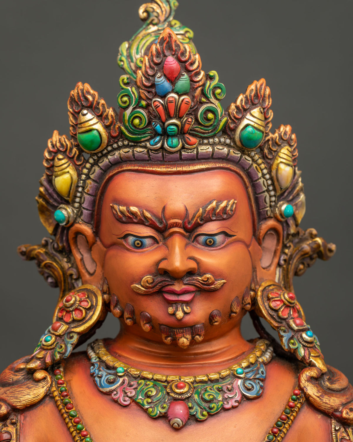 Face of Yellow Dzambhala statue with semi-wrathful expression, gemstone-set crown and gold gilding
