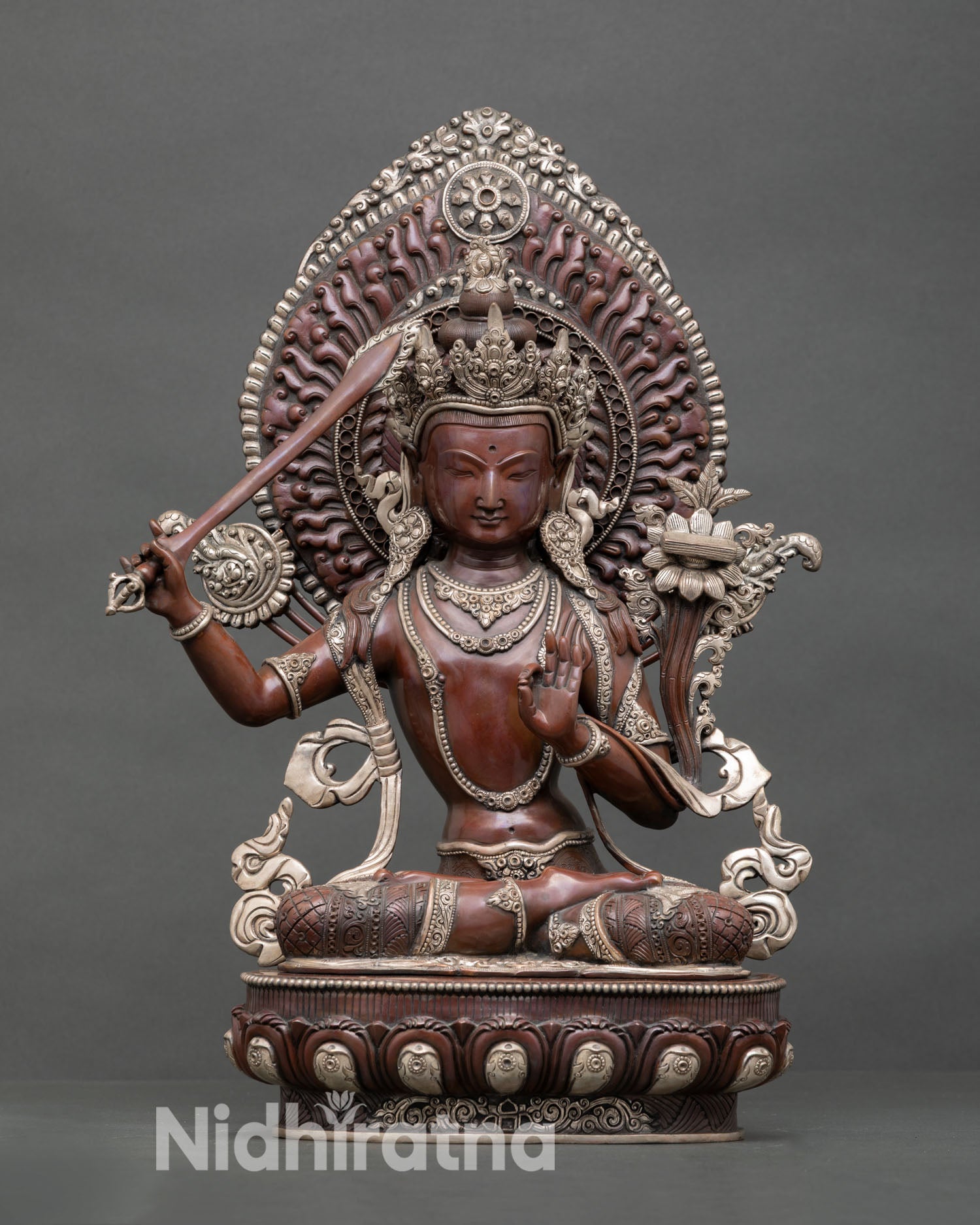 Front view of Manjushri statue handcrafted by Newari artisan in Nepal oxidized copper, seated on lotus throne with silver plated detailing and radiant halo
