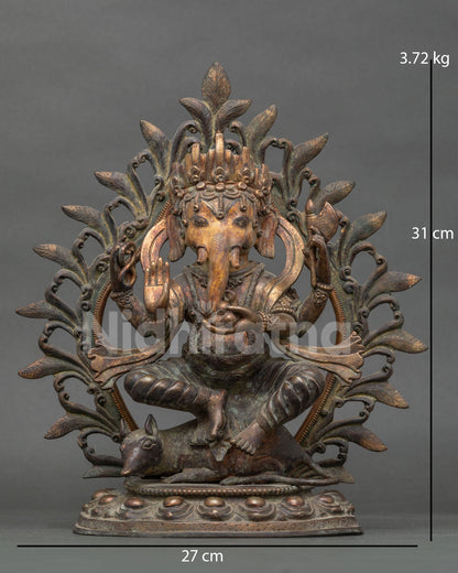 Front view of four-armed oxidized copper Ganesha statue seated on Mushaka rat within a halo