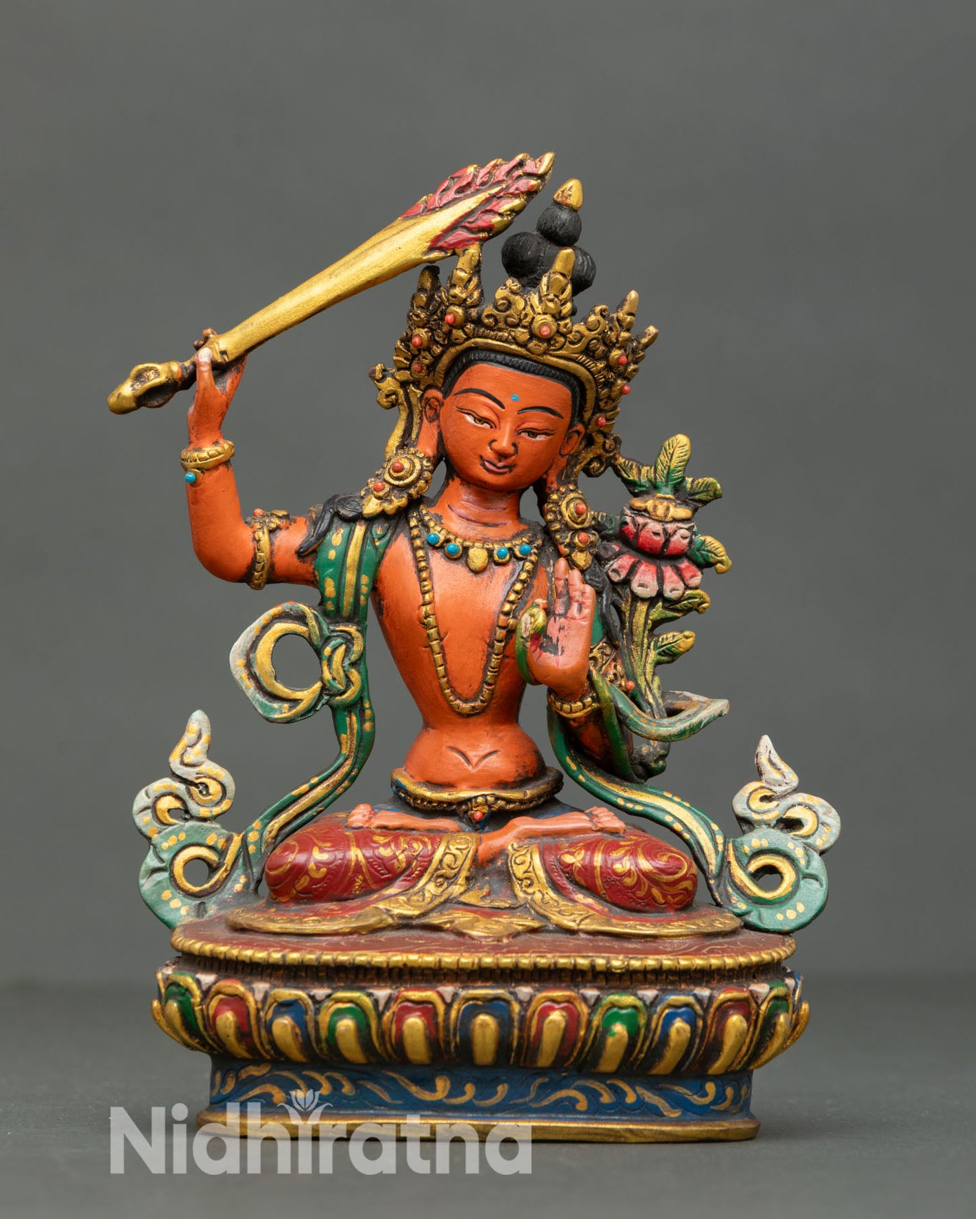 Front view of handcrafted Manjushri statue from Nepal in copper lost wax casting with acrylic detailing and semi precious stones seated on lotus pedestal
