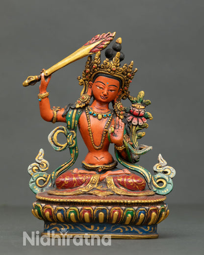 Front view of handcrafted Manjushri statue from Nepal in copper lost wax casting with acrylic detailing and semi precious stones seated on lotus pedestal