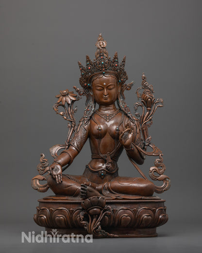 front view of oxidized green tara statue seated in royal ease on lotus base
