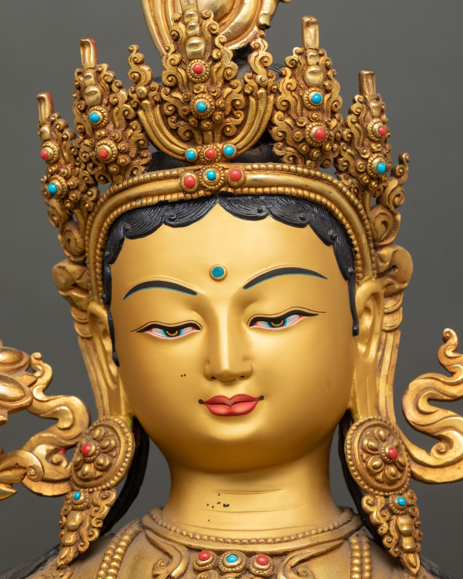 Gold-painted face of Green Tara statue with five-jeweled crown and compassionate expression