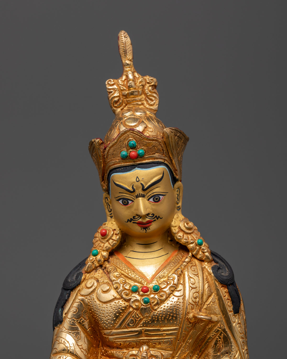 Gold-painted face and ornate details of a handcrafted Guru Rinpoche Buddhist statue